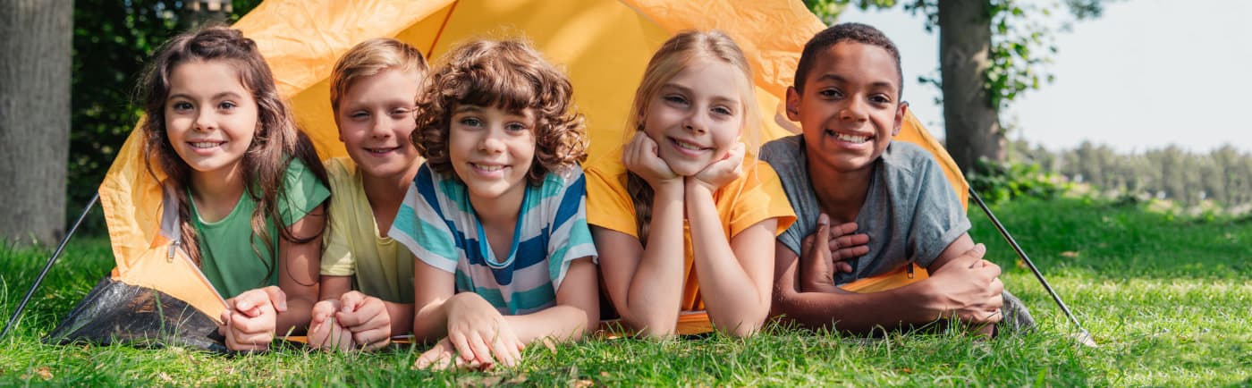 panoramic shot of happy multicultural kids smiling while lying near camp